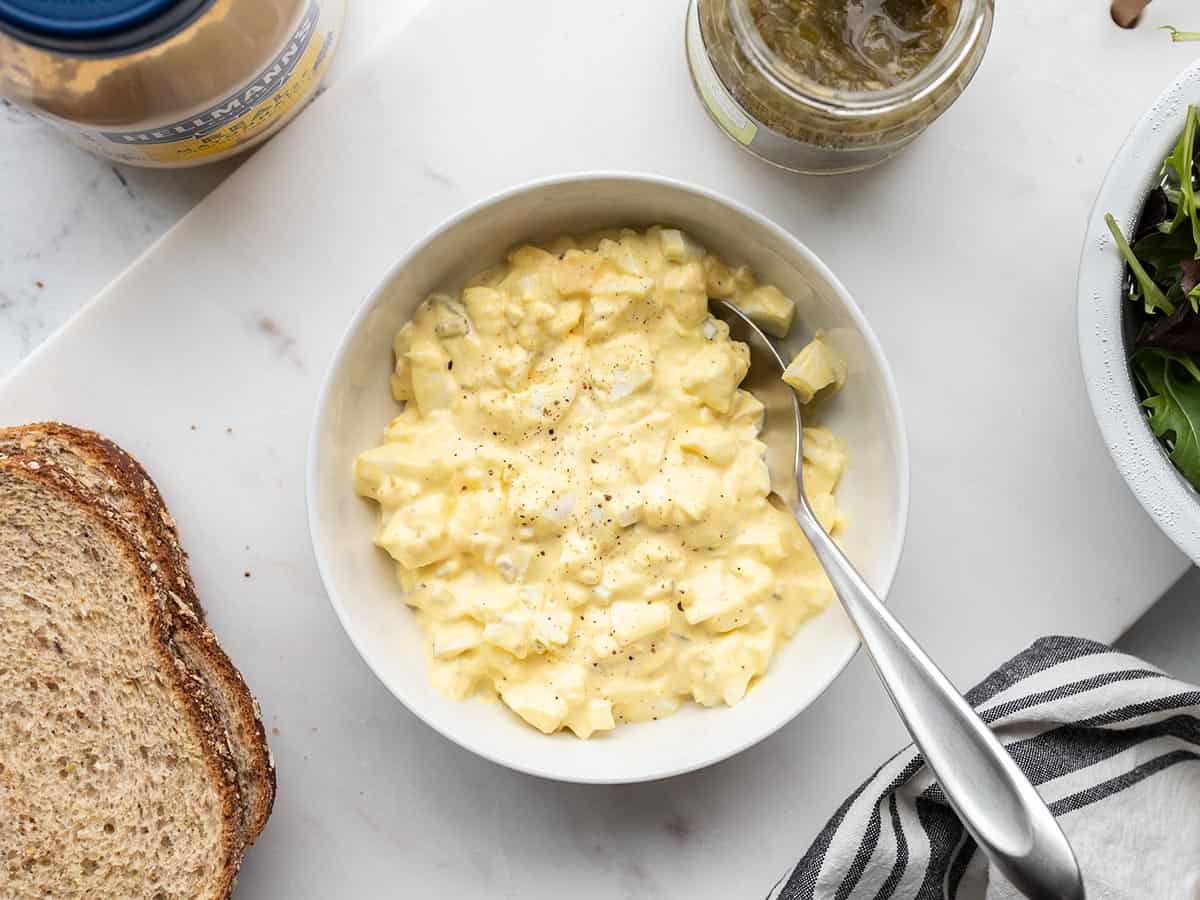 A bowl of egg salad with ingredients on the sides