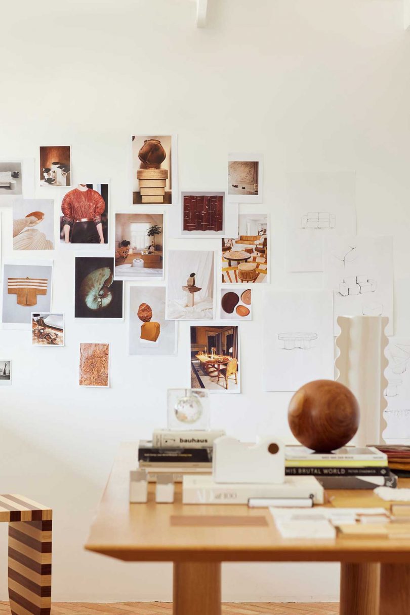 Photos and sketches hang randomly on a white wall in a design studio