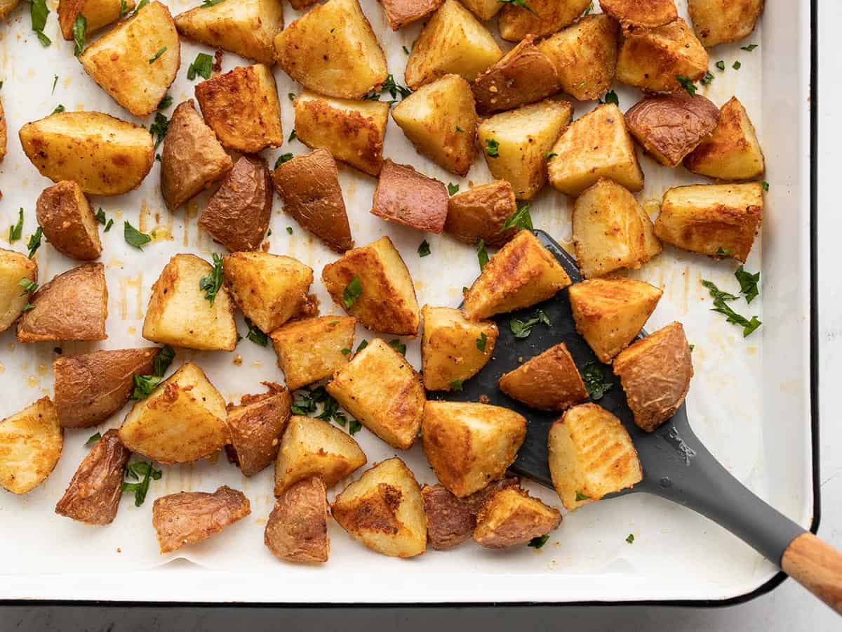 Parmesan Roasted Potatoes on a baking sheet being scooped up with a spatula