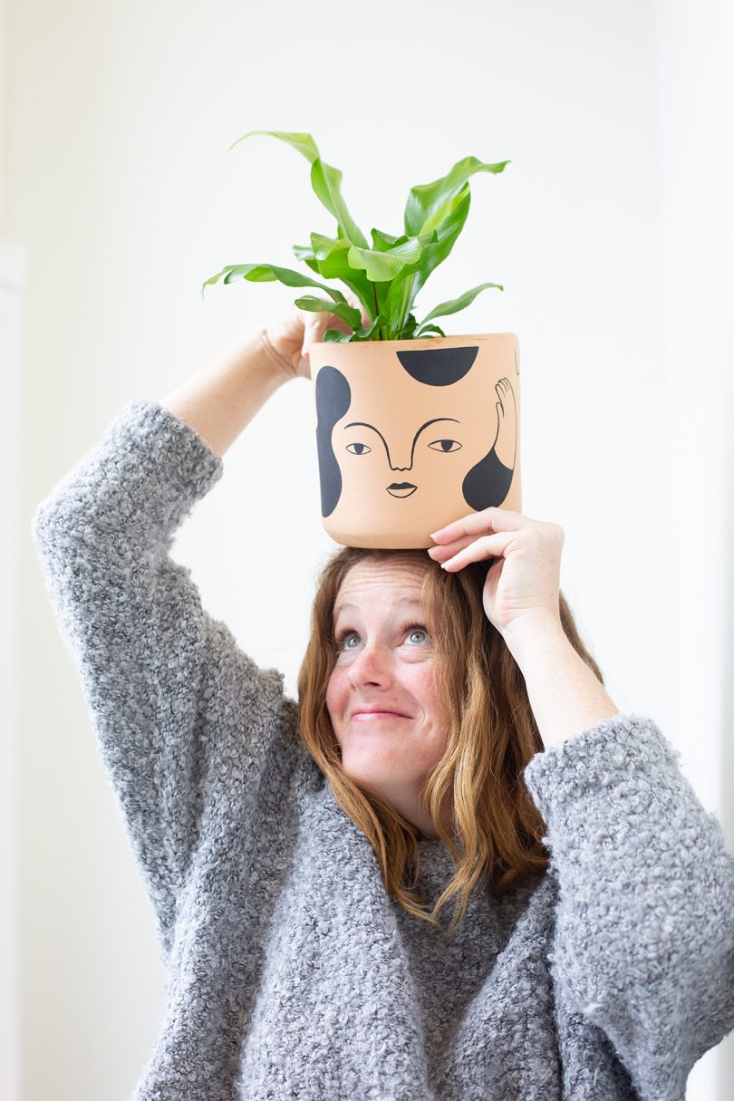 light-skinned woman balancing a potted plant on her head