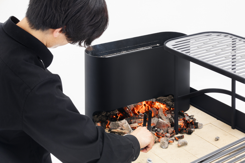 person spreading coals on a black grill