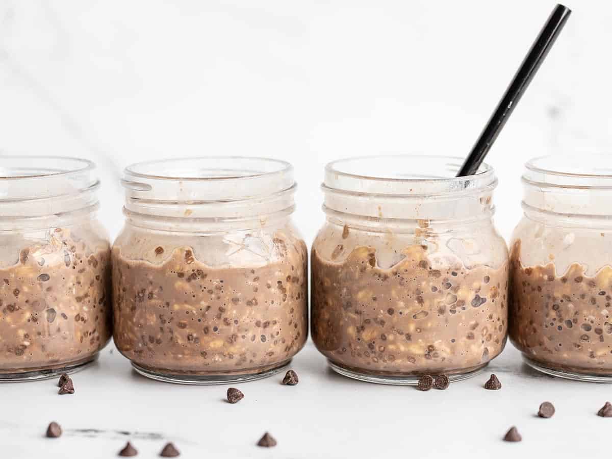 Side view of four jars of overnight oats with a spoon in one.