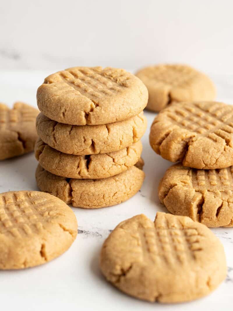 A stack of peanut butter cookies with a few scattered around.