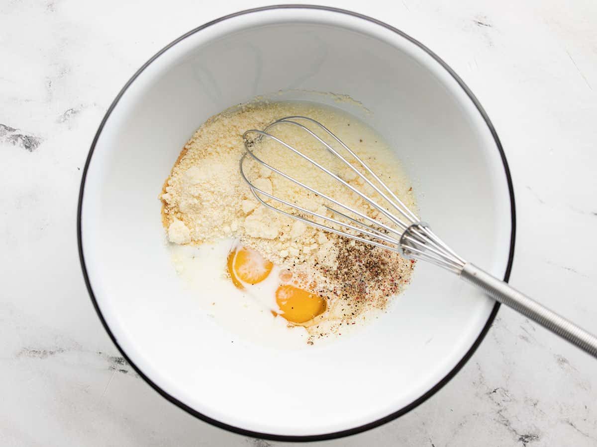 eggs, cheese, and milk in a bowl with a whisk.