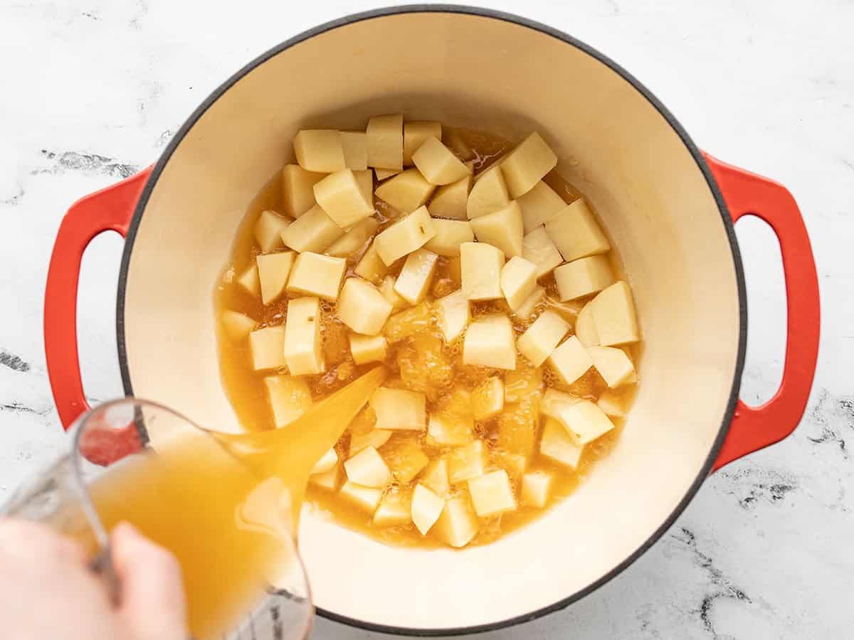 broth being poured into a pot with cubed potatoes.
