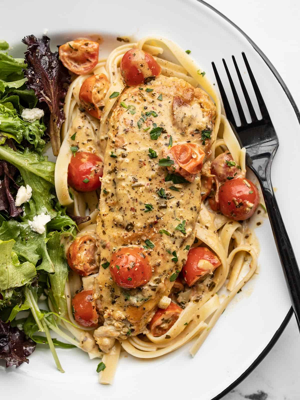 Creamy pesto chicken on a plate with pasta and a salad.