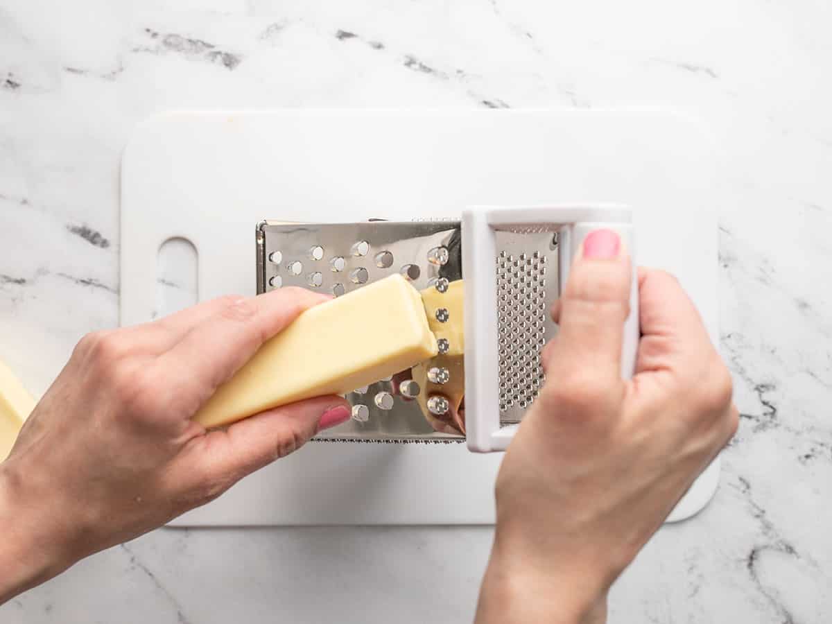 Overhead shot of a hand grating butter on a box grater.